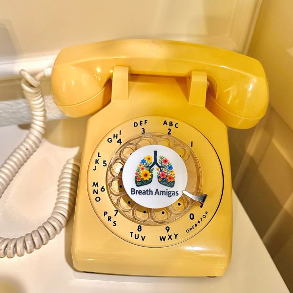 Vintage yellow rotary telephone featuring the colorful Breath Amigas logo.