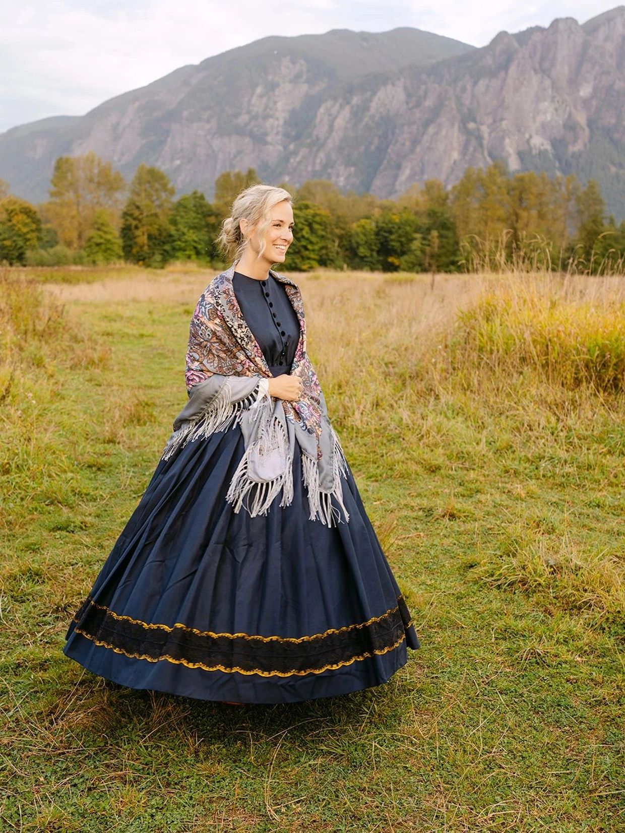 Woman in traditional dress smiles in a mountain meadow.