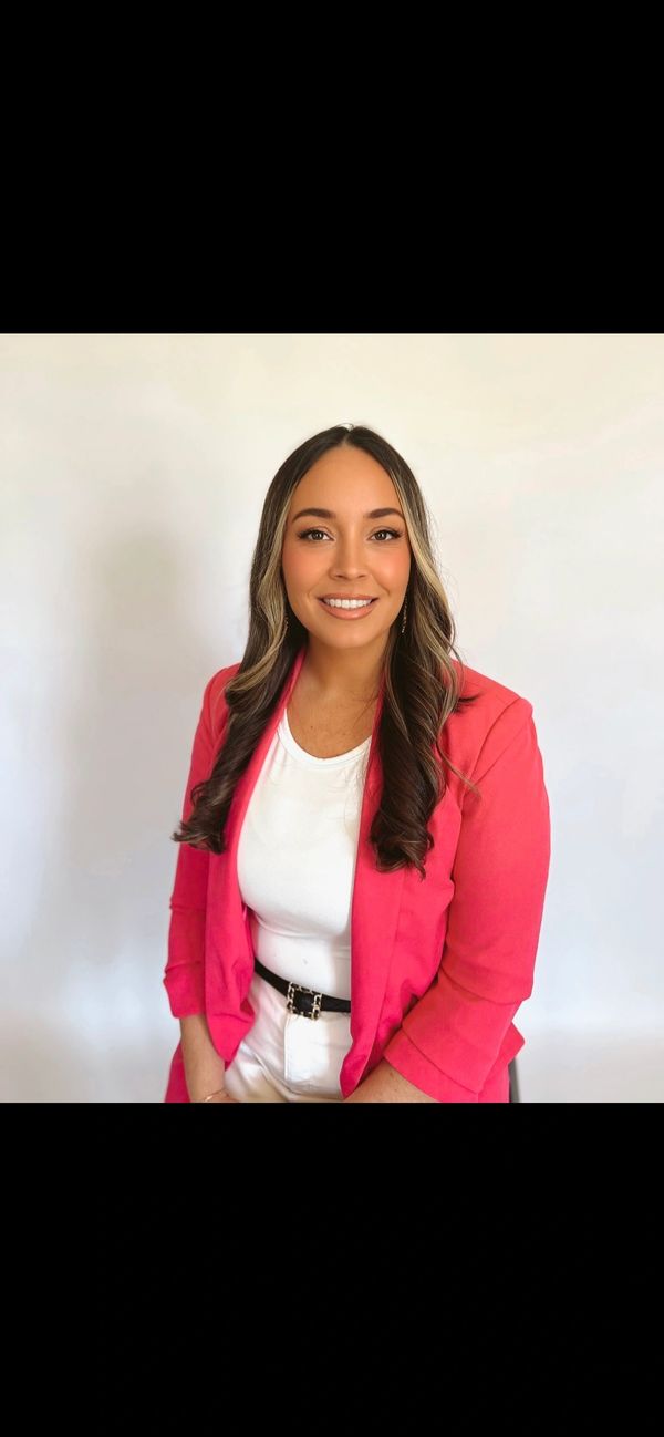 A smiling woman in a white top and pink blazer against a plain background.