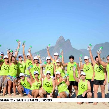 Group of fitness enthusiasts in matching green shirts posing on Ipanema beach with water bottles.