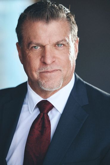 Confident middle-aged man in a dark suit and red tie.