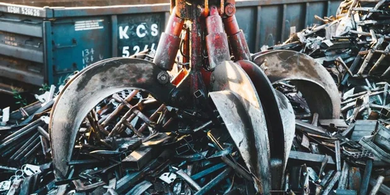 Industrial claw machine lifting scrap metal in a junkyard.