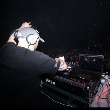 DJ performing live with headphones in front of a crowd.