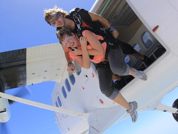 Two people preparing to skydive from a plane under a bright sun.