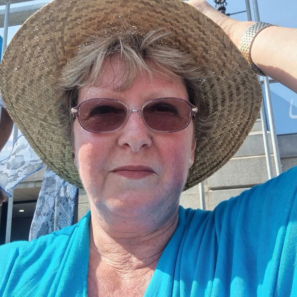 Woman wearing a straw hat and pink sunglasses outdoors.
