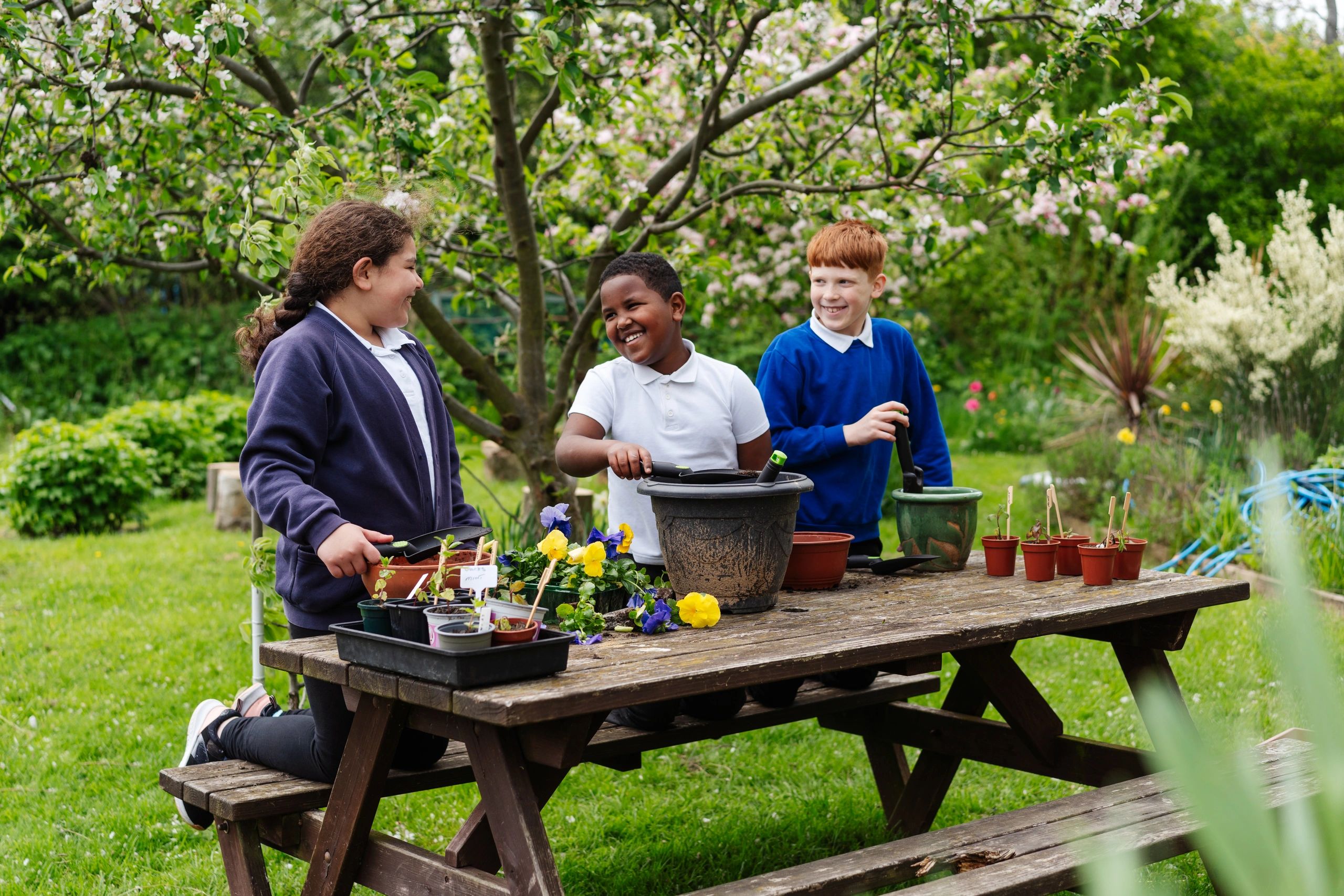 Children gardening and smiling at a picnic table outdoors.