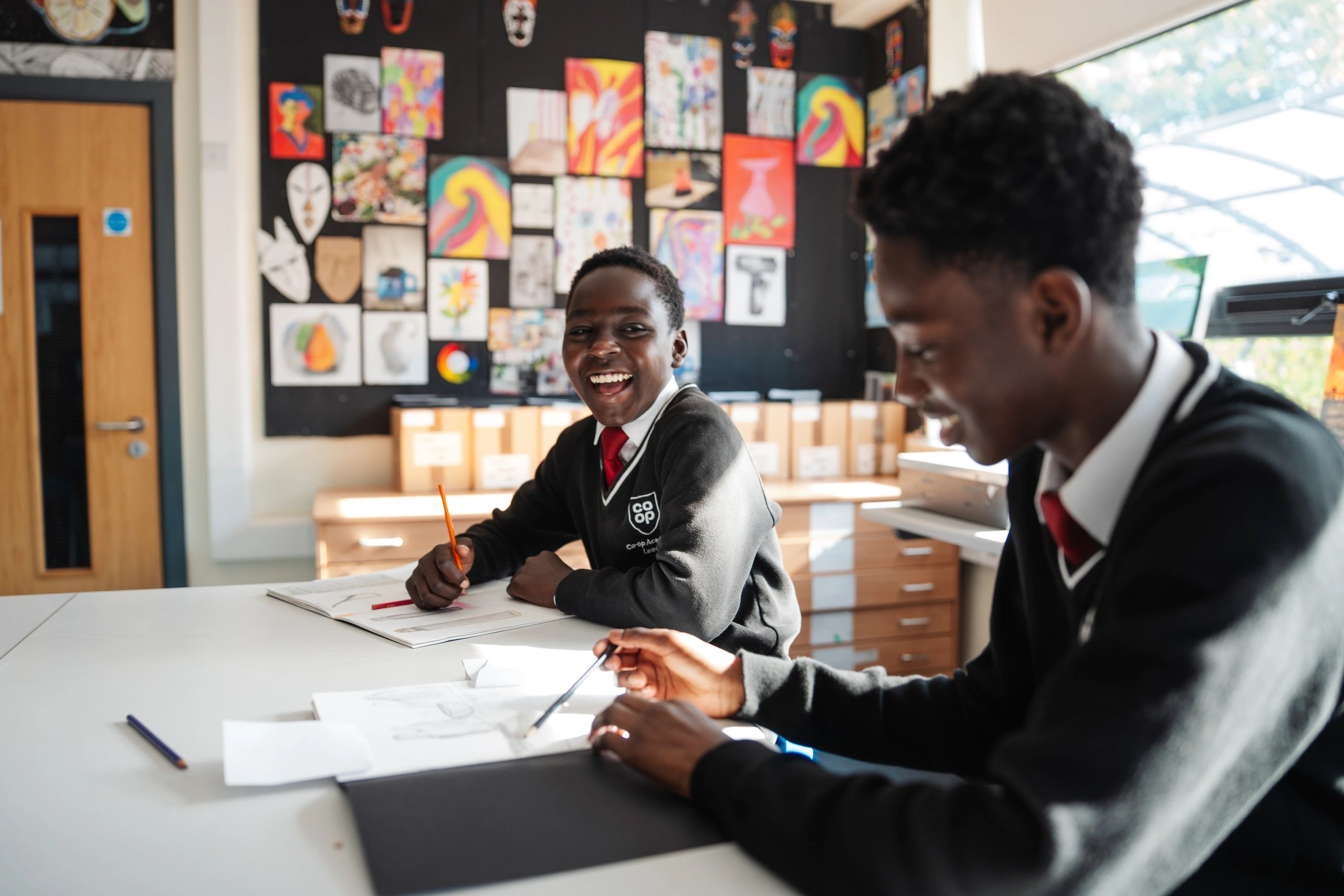 Two students smiling and drawing in a colorful classroom.