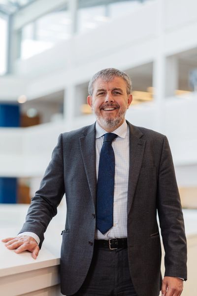 Smiling businessman in a suit standing indoors with a modern office background.