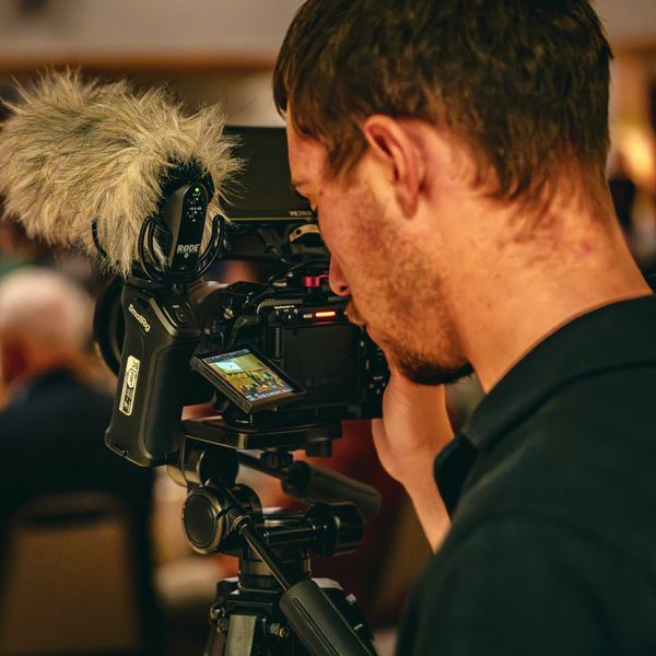 A man filming with a professional camera and microphone on a tripod.