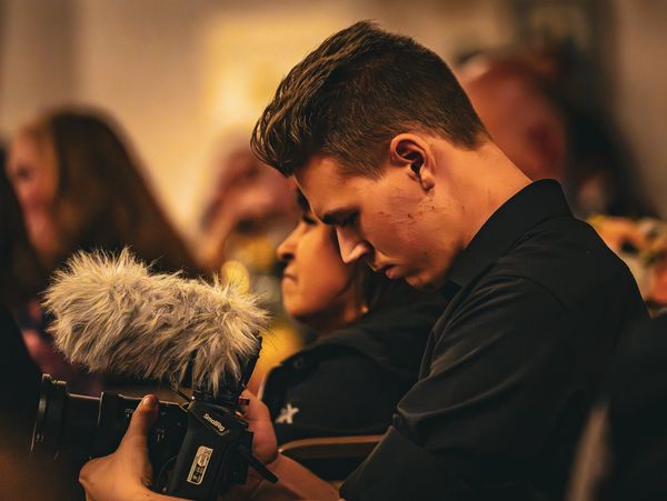 A man focuses intently on adjusting a professional camera with a furry microphone.