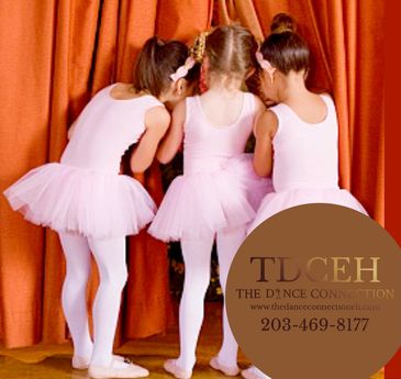 Three young ballerinas in pink tutus whispering backstage.