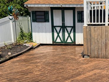 A wooden deck and a white shed with green shutters in a backyard.