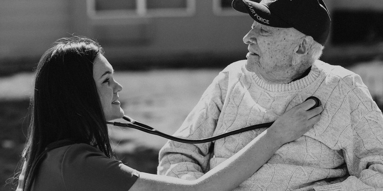 A nurse checks an elderly man's heart with a stethoscope outdoors.