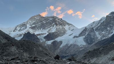 Snow-covered mountain peak during sunrise with rocky foreground.