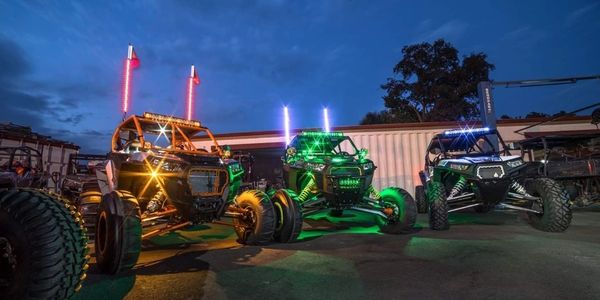 Three off-road vehicles with colorful LED lights parked at night.