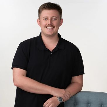 Man in black shirt smiling with arms resting on chair.