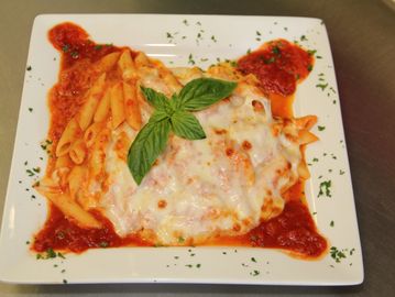Penne pasta with melted cheese and tomato sauce, garnished with basil on a white square plate.