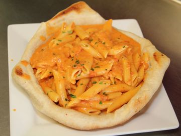 Creamy penne pasta served in an edible bread bowl on a white plate.