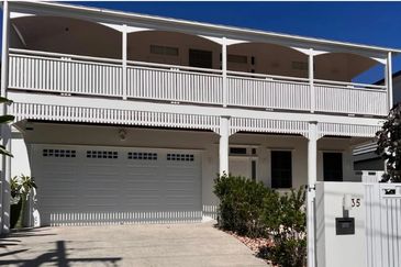 Two-story white house with a spacious balcony and garage under a clear blue sky.