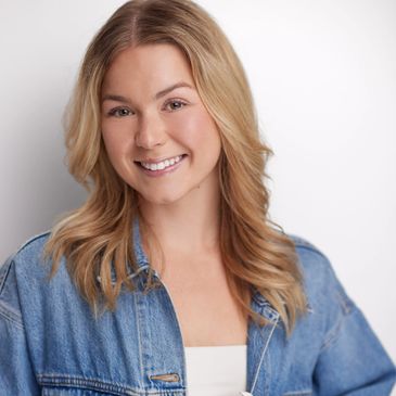 Smiling young woman with blonde hair in denim jacket.