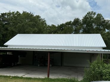 A large carport with white metal roofing and garage behind it.