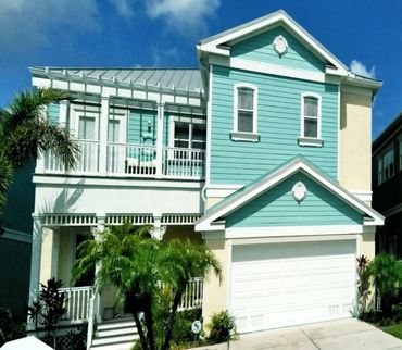Bright blue and white two-story house with lush palm trees and a garage.
