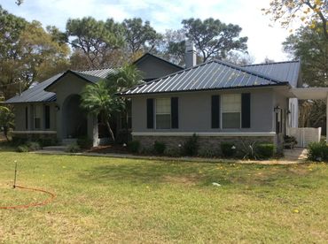 Gray house with metal roof and lush green lawn in front.
