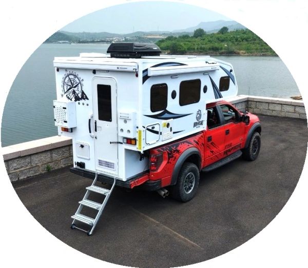 Red pickup truck with a white camper parked by a waterfront.