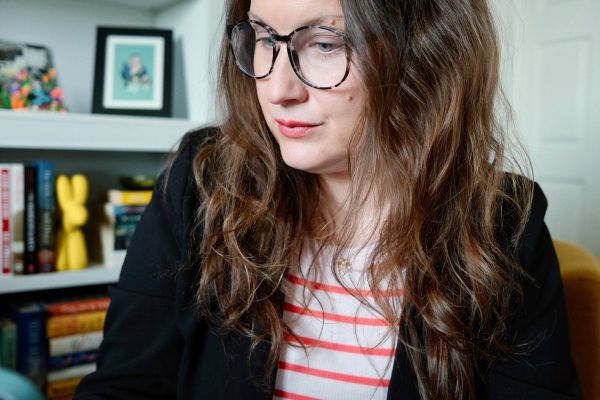 Woman with glasses looking down, wearing a striped shirt and black jacket.