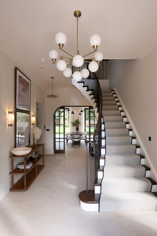Elegant hallway with a curved staircase and modern chandelier.
