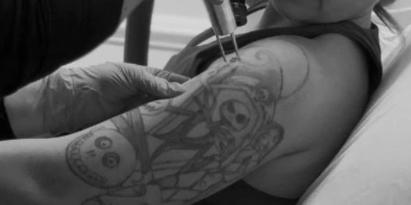 A person getting a tattoo on their upper arm with a machine.