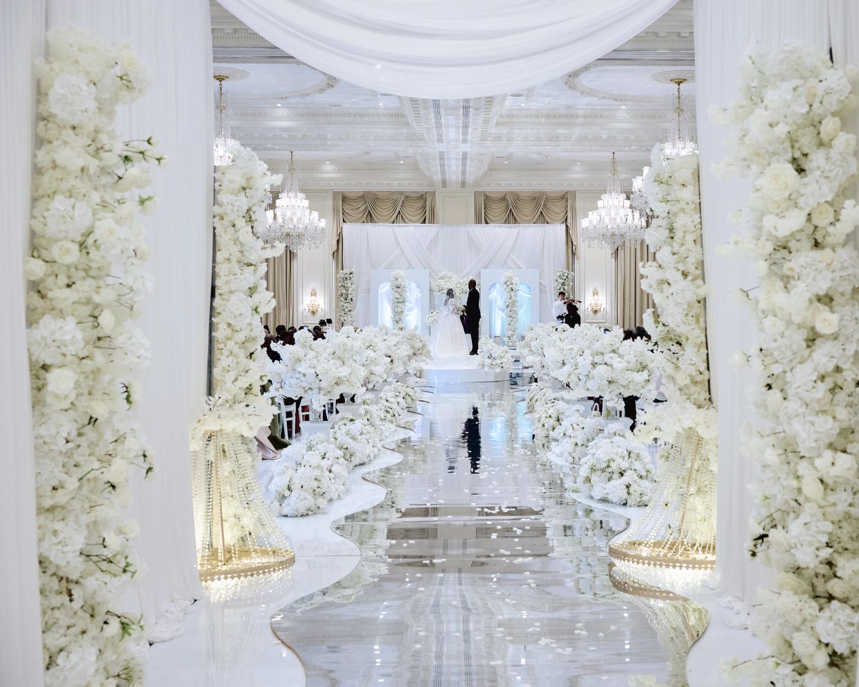 Luxurious white-themed wedding ceremony with elegant floral arrangements and chandeliers.
