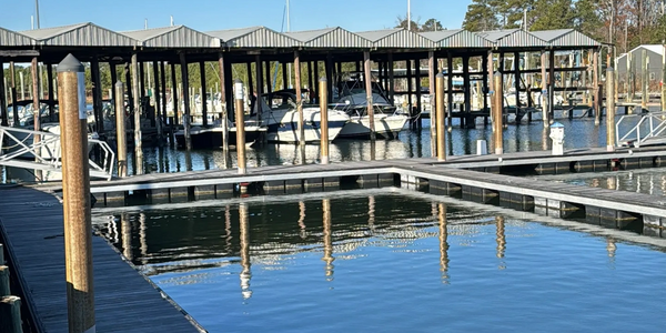 Boats docked under covered slips at a calm marina on a clear day.