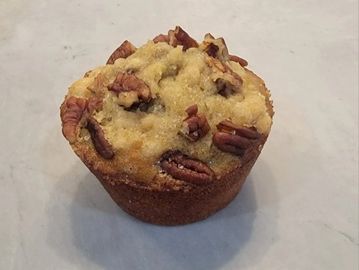 A muffin topped with pecans on a marble surface.