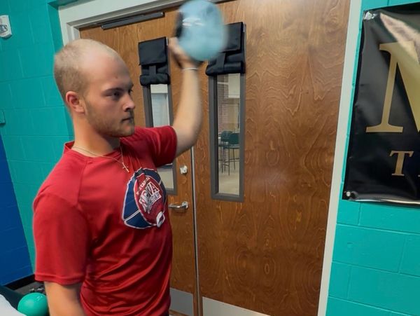Young man in red shirt holding a kettlebell in a gym room.