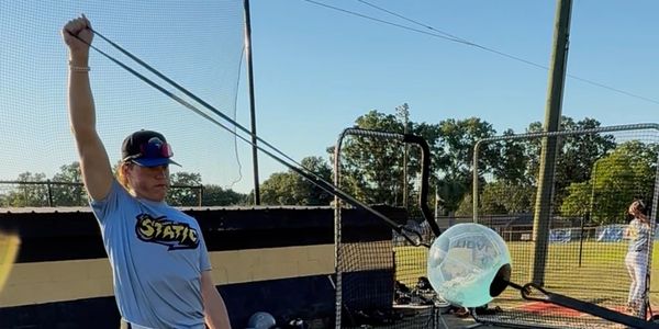 A baseball player practices swing with a training ball attached to a stretch cord.