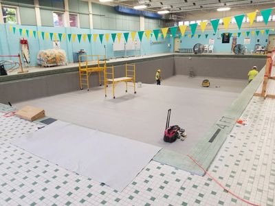 Crew working inside an empty indoor commercial pool during renovation.