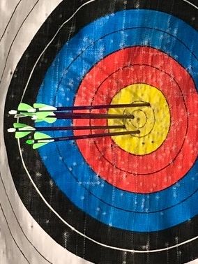 Five arrows grouped tightly in the yellow center of an archery target.