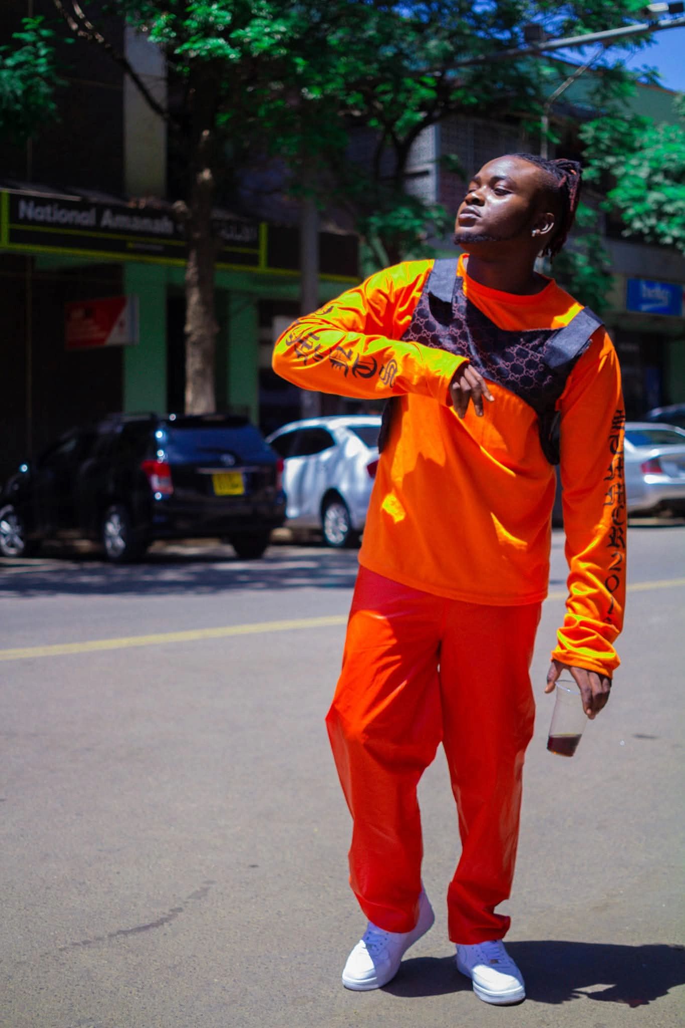 Man in bright orange outfit with white sneakers holding a drink on the street.