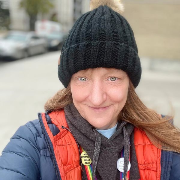 Smiling woman in winter clothing with a black knit hat and puffy jacket.