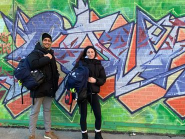 two people in winter attire posing in front of a graffiti wall