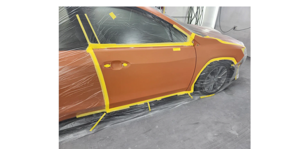 orange car shown taped off with yellow tape during the painting and refinishing process 