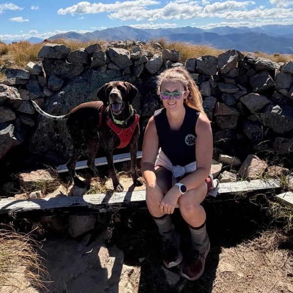 Woman and dog resting on a mountain trail with rocky backdrop.