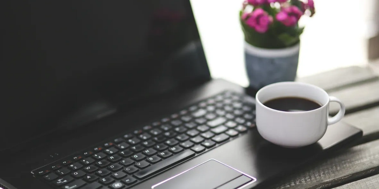 Laptop keyboard with a coffee cup and a small potted plant on a wooden surface.