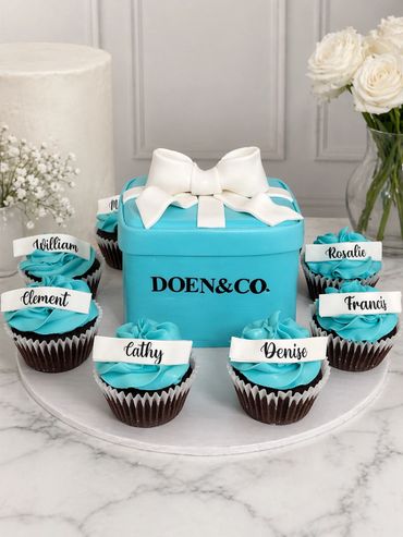 Elegant turquoise gift box cake with personalized name cupcakes arranged around it.