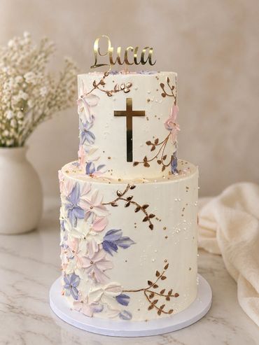 Elegant two-tier cake with floral decorations and a cross for a religious celebration.
