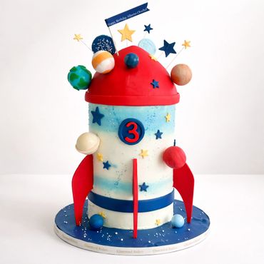 A colorful space-themed rocket birthday cake adorned with planets and stars.