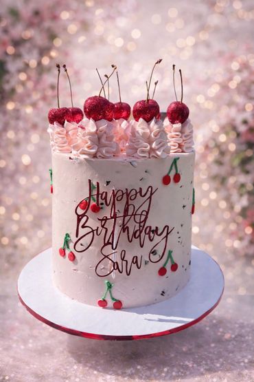 Elegant birthday cake decorated with cherries and pink frosting.