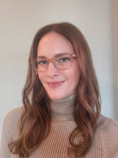 Woman with glasses and a beige turtleneck smiling.