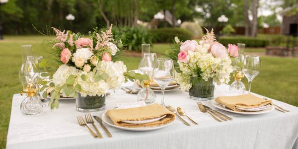 Elegant outdoor table setting with floral centerpieces and glass lanterns.